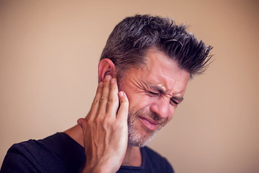 adult man holding his ear in pain, symptoms of TMJ