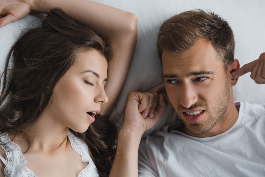 young adult woman snoring while partner plugs his ears